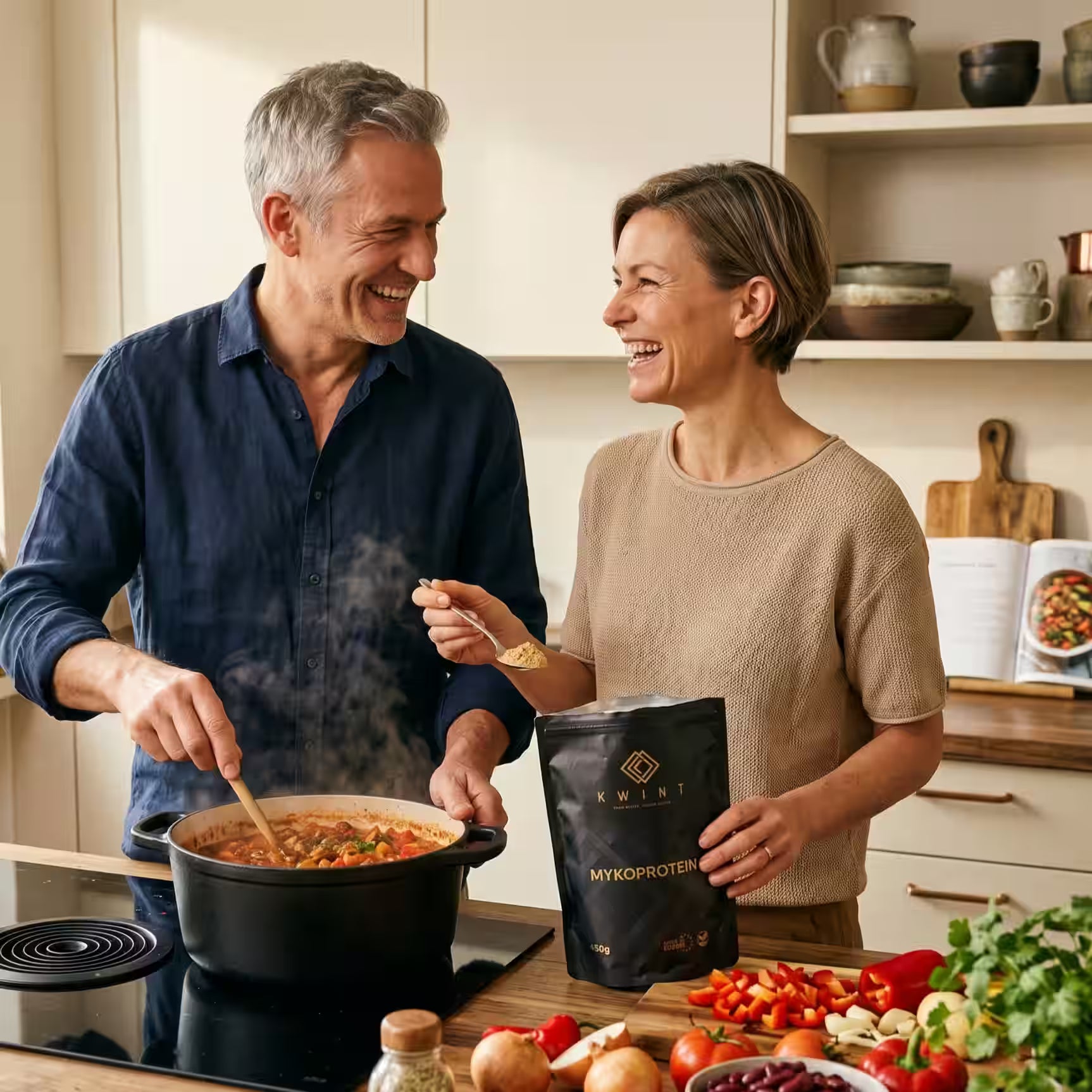 älteres Paar, in der Küche ein Chili kochend. Die Dame hält eine Packung Kwint Mykoprotein in der Hand und fügt einen Löffel zum Topf hinzu.