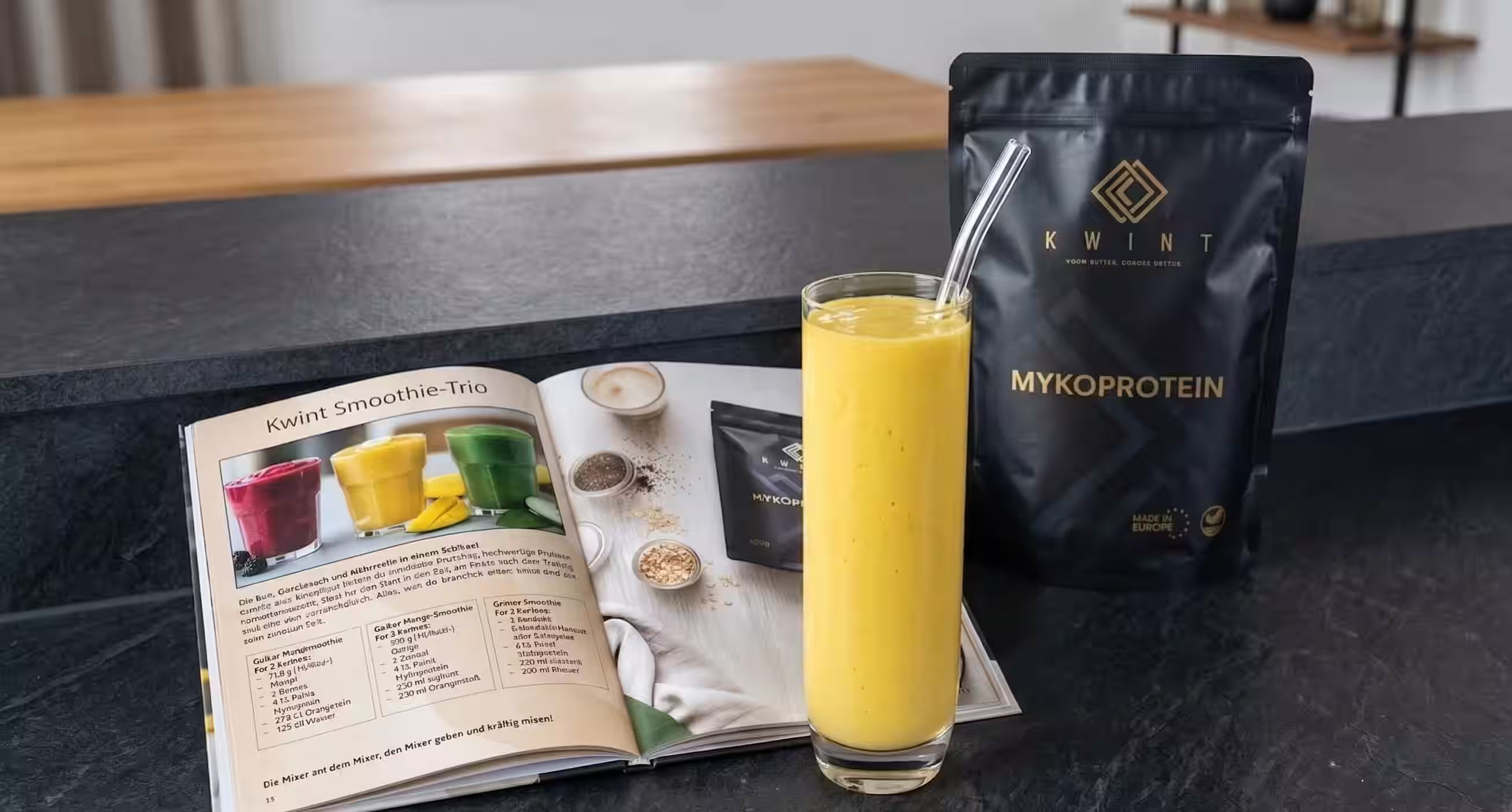 Ein Beispielbild, wie Kwint Mykoprotein in einem gelben Smoothie verwendet werden kann. Der Smoothie, das Kochbuch und eine Packung Kwint Mykoprotein sind auf einer schwarzen Anrichte zu sehen.