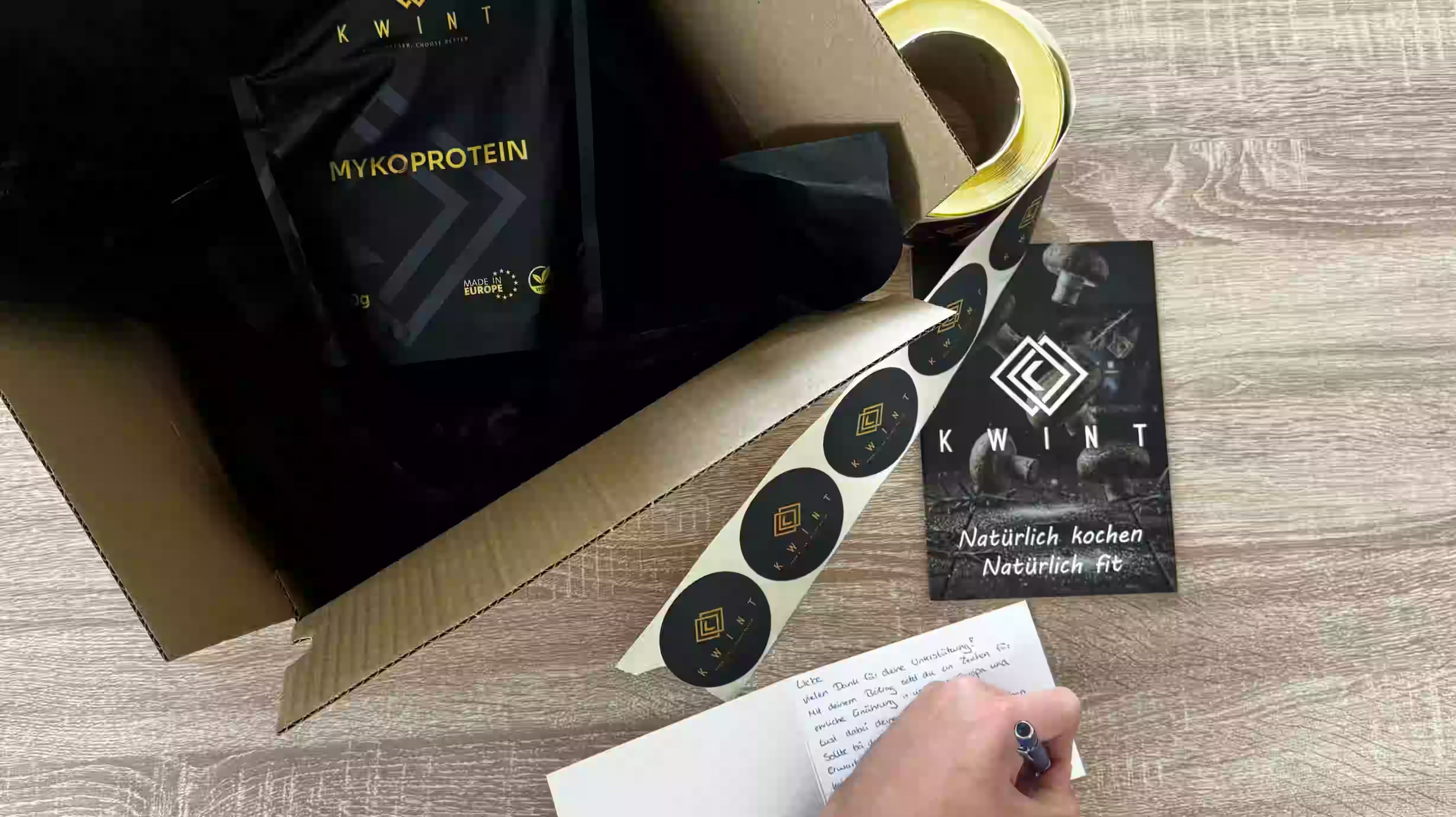 eine Beispielszene, wie eine Packung Kwint Mykoprotein für den Versand bereit gemacht wird. Einer der Gründer schreibt eines Dankeskarte und das Kochbuch ist zu sehen.